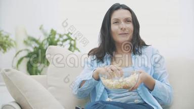 慢点。 一个可爱的女人，一边吃着爆米花，一边惊讶地看电视。 好吃-好吃。 4K.